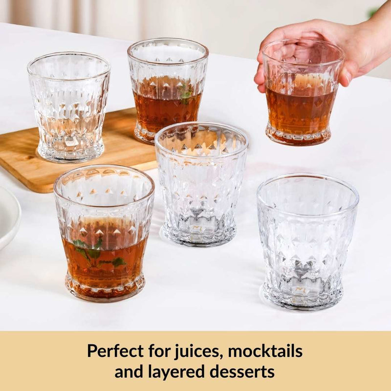 Clear glasses with layered drinks on a white surface, with a hand holding one glass.