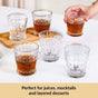 Clear glasses with layered drinks on a white surface, with a hand holding one glass.